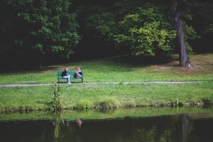 two people sitting in the distance on a park bench with a lake in front 